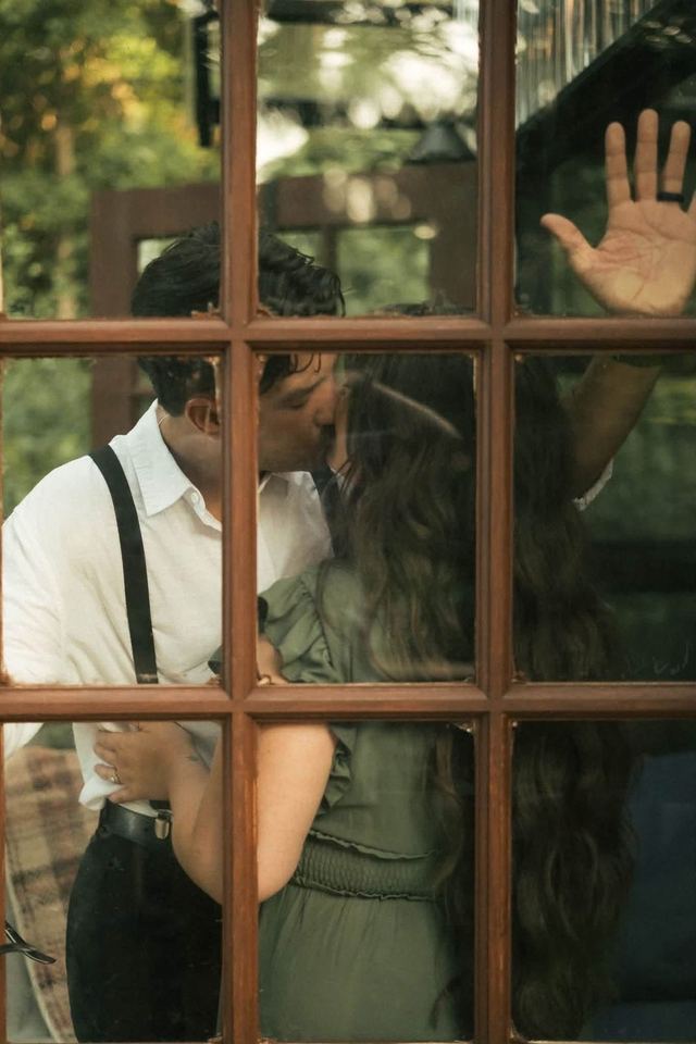 A couple kissing, seen through the panes of The Glasshouse French doors